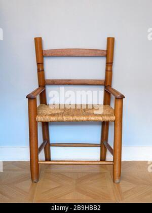 Petite chaise en bois et en osier vintage isolée sur un mur de chambre de bébé peint en bleu pâle. Banque D'Images