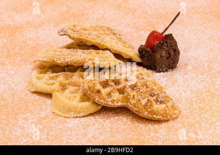 Triangle de gaufres maison avec sucre en poudre, une boule de glace au chocolat et une cerise sur fond rose, image isolée de la nourriture. Banque D'Images