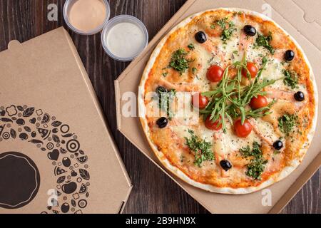 Pizza à croûte mince avec saumon aux fruits de mer et roquette dans une boîte de livraison de carton Banque D'Images