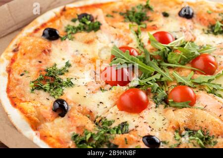 Pizza italienne savoureuse dans une boîte en carton près. Pizza avec fruits de mer, saumon, tomates et roquette Banque D'Images