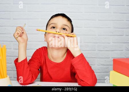 Énervé ennuyant l'école qui fait des devoirs. Enfant fatigué de faire des devoirs étudier avec le stylo sur les livres ouverts. Enfant surchargé. Retour à l'école. Apprentissage à distance Banque D'Images