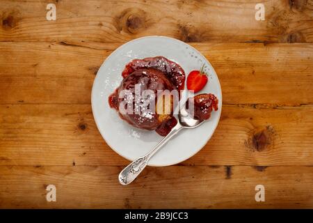 Un gâteau éponge de fraise individuel, avec une sauce aux fraises collantes, sur une plaque blanche avec une cuillère, sur une surface en bois avec un espace de copie Banque D'Images