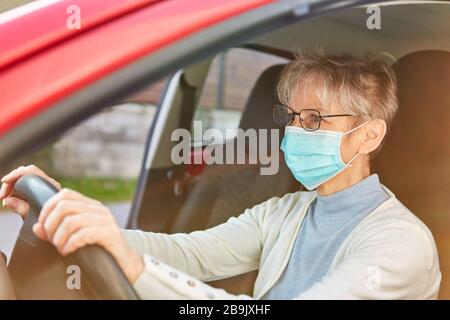 Femme âgée avec masque de visage conduisant une voiture pendant l'épidémie de coronavirus Banque D'Images