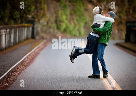 Homme levant la femme dans l'air sur la route Banque D'Images