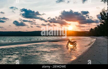 Une moto argentée se trouve sur la plage au coucher du soleil Banque D'Images