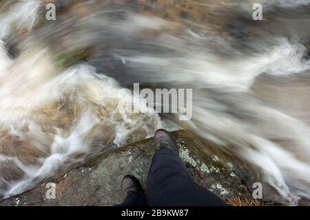 Walker est sur le point de traverser l'eau en mouvement rapide après de fortes pluies dans la campagne, Burley Moor, Yorkshire, Angleterre, Royaume-Uni Banque D'Images