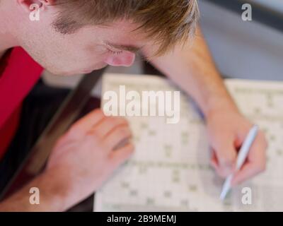 Gros plan d'un homme tenant un crayon à la résolution des mots croisés portant un maillot rouge dans son temps libre. Banque D'Images