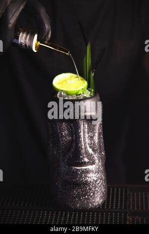 Cocktail de boissons Tiki au bar. Barman avec gants décorent la boisson avec de l'orange sec. Banque D'Images