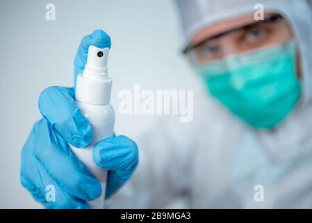 Un médecin caucasien dans un costume de protection et un masque chirurgical utilise de l'aseptisant pour le coronavirus. Mains mâles tenant un gel antibactérien. Mesures préventives ag Banque D'Images