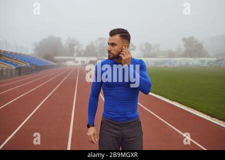 Guy avec une barbe avec écouteurs debout au stade le matin Banque D'Images
