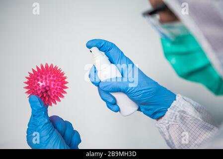 Un médecin caucasien dans une combinaison de protection et un masque chirurgical utilise un désinfectant pour le modèle rouge de Coronavirus. Main mâle tenant un gel antibactérien. Méas. Préventives Banque D'Images
