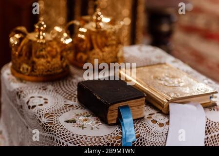 Mariage des couronnes d'or et de la bible sur la table dans l'église. Couronnes de mariage dans l'église prêtes pour la cérémonie de mariage. Gros plan. Liturgie divine. Sélective Banque D'Images