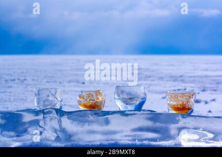 Quatre verres en support de glace sur un morceau de glace transparente contre une plaine enneigée et un ciel bleu. Concentrez-vous sur la glace et les verres. L'arrière-plan est flou. Banque D'Images