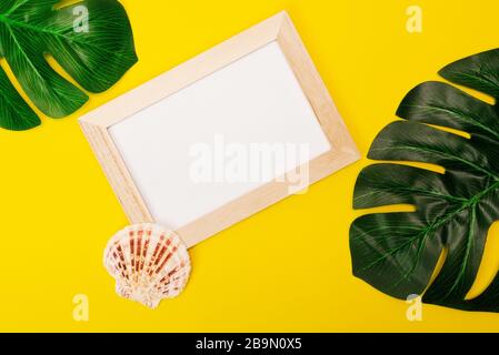 maquette tropicale avec cadre photo blanc et feuilles de palmier sur fond jaune coloré. Cadre photo avec un endroit vide pour le texte ou la publicité avec des coquillages sur un fond jaune. Banque D'Images