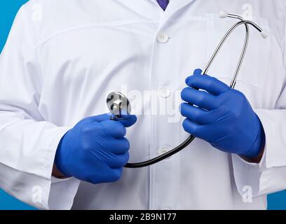 le médecin adulte masculin dans un manteau médical blanc est debout et possède un stéthoscope noir sur un fond bleu, gros plan Banque D'Images