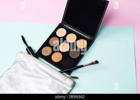 Un petit sac cosmétique argent avec une large palette noire de tons neutres neutres neutres, une brosse mascara et une brosse pour l'application de cosmétiques sur un fond pastel. Le concept de maquillage quotidien rapide. Banque D'Images