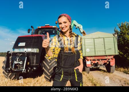 Femme paysanne devant une machine agricole donnant des pouces Banque D'Images