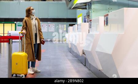 Femme avec porte-bagages à des comptoirs d'enregistrement presque vides au terminal de l'aéroport en raison des restrictions de voyage liées à l'éclosion de coronavirus pandémique/Covid-19. Banque D'Images