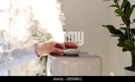 La femme s'allume et inhale la vapeur d'huile aromatique de l'humidificateur. Technologie ultrasonique, augmentation de l'humidité de l'air à l'intérieur, conditions de vie confortables dans Banque D'Images