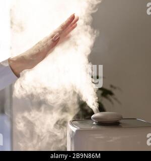 La femme tient la main sur le diffuseur d'huile d'arôme de vapeur sur la table à la maison, la vapeur de l'humidificateur d'air. Technologie ultrasonique, augmentation de l'humidité de l'air dans Banque D'Images