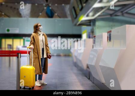 Femme avec porte-bagages à des comptoirs d'enregistrement presque vides au terminal de l'aéroport en raison des restrictions de voyage liées à l'éclosion de coronavirus pandémique/Covid-19. Banque D'Images