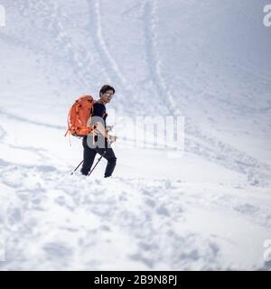 Sports d'hiver - jeune homme marchant avec des raquettes/des skis de randonnée dans les hautes montagnes couvertes de beaucoup de neige (foyer sélectif sur la montagne dans le dos Banque D'Images