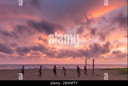 Jeunes hommes jouant au football social sur la plage au coucher du soleil à Negombo, Sri Lanka Banque D'Images