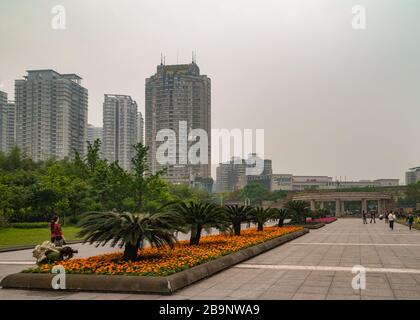 Chongqing, Chine - 9 mai 2010 : grands lits à fleurs orange et rouge au centre d'un large passage juste à l'intérieur du zoo. Les gratte-ciel contre le ciel argenté sont re Banque D'Images