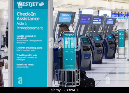 Toronto, Canada. 24 mars 2020. Un voyageur saisit sa carte d'embarquement dans la zone de service express d'enregistrement WestJet de l'aéroport international Pearson de Toronto, Canada, le 24 mars 2020. La deuxième compagnie aérienne du Canada WestJet a annoncé mardi la mise à pied de 6 900 employés en raison de l'impact de la pandémie de COVID-19. Près des deux tiers de la flotte de 120 avions de la compagnie aérienne sont actuellement mis à la terre. Crédit: Zou Zheng/Xinhua/Alay Live News Banque D'Images