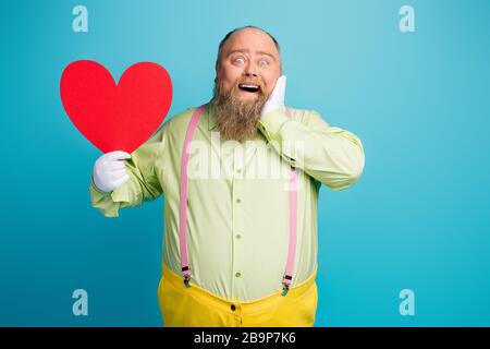 Portrait de son beau drôle drôle funky rêveuse gaie gaie homme enchanté tenant dans la main grand coeur en appréciant le 14 février isolé sur lumineux Banque D'Images