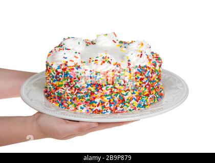 De jeunes mains caucasiennes tenant un gâteau à la vanille avec de la crème fouettée géliante recouverte de bonbons saupoudrer sur une plaque en porcelaine isolée sur blanc. Bi festif Banque D'Images