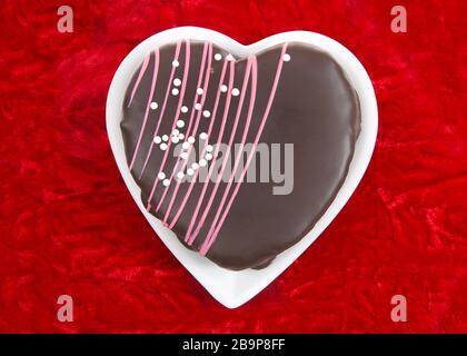 Gâteau au chocolat au coeur sur une plaque en forme de coeur blanche posée sur un fond de velours rouge. Dessert sur le thème de la Saint-Valentin Banque D'Images