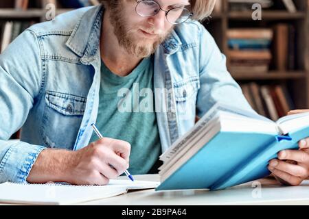 Les jeunes étudiants de la bibliothèque au bureau prennent des notes. Banque D'Images