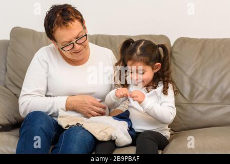 Grand-mère enseigne à sa petite-fille à porter des vêtements. Pas d'endroit comme à la maison. Vêtements, moments de famille confortables, vie durable, shopping moins concept. Banque D'Images