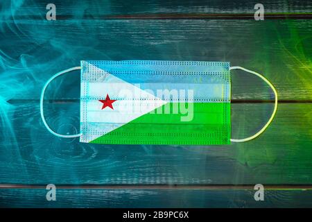 Masque médical pour la protection contre les maladies aéroportées, peint dans le drapeau national de Djibouti sur un fond noir dans la fumée bleu-vert. PR. Médicale Banque D'Images