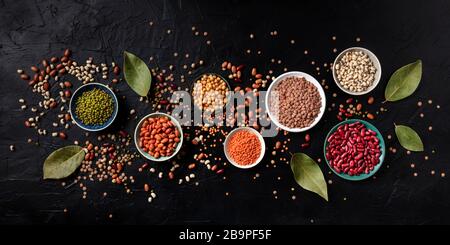 Légumineuses panorama, tiré du dessus sur un fond noir. Lentilles, soja, pois chiches, haricots rouges, une vatiété des légumineuses Banque D'Images