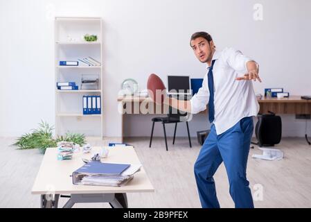 Jeune employé jetant du ballon de rugby dans le bureau Banque D'Images