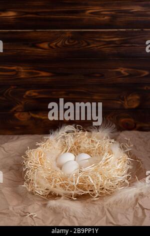 Les œufs de poulet se trouvent sur une paille de papier méchant dans un panier en osier sur un fond en bois sombre au soleil du matin Banque D'Images