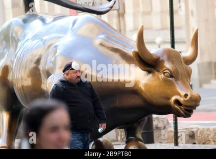 New York, New York, États-Unis. 24 mars 2020. Un homme passe devant le taureau de chargement de Wall Street à New York, aux États-Unis, le 24 mars 2020. Le nombre de cas de COVID-19 aux États-Unis a dépassé 50 000 à 15 heures, heure de l'est des États-Unis, mardi (1900 GMT), selon le Centre for Systems Science and Engineering (CSSE) de l'Université Johns Hopkins. Le chiffre frais a atteint 50 206 avec 606 morts, a déclaré le CSSE. L'état de New York est devenu l'épicentre de l'épidémie COVID-19 dans le pays, avec 25 665 cas signalés. Crédit: Wang Ying/Xinhua/Alay Live News crédit: Xinhua/Alay Live Nouveau Banque D'Images