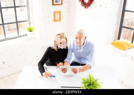 Prise de vue haute angle de Happy senior couple shopping en ligne. Jolie femme âgée tenant une carte bancaire dans sa main tandis que l'homme senior assis derrière son l Banque D'Images