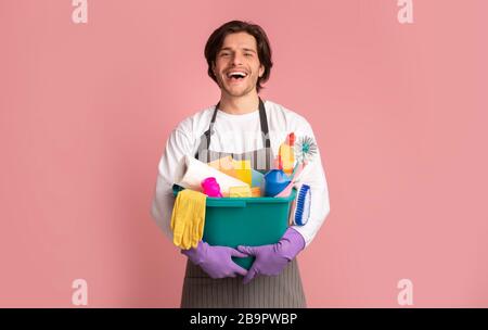 Joyeux jeune homme tenant seau avec des fournitures de nettoyage, fond rose studio Banque D'Images