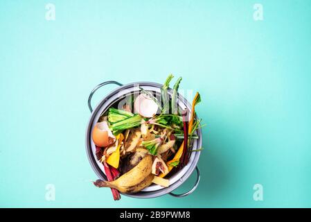 Légumes pelés sur la planche à découper, bac à compost blanc sur fond bleu. Vue de dessus des déchets alimentaires de cuisine collectés dans le recyclage du pot de compost Banque D'Images