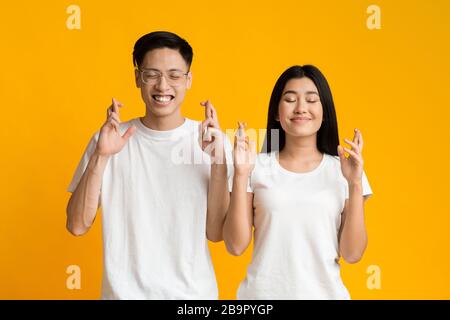 Un jeune couple asiatique ferme les yeux et croise les doigts avec espoir Banque D'Images