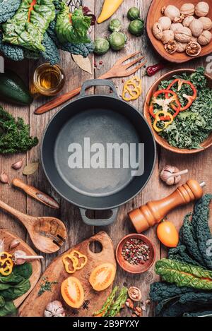 Divers ingrédients de légumes biologiques et un pot de cuisine vide en fer, des bols en bois, des cuillères sur fond en bois. Vue de dessus, espace de copie. Légumes biologiques Banque D'Images