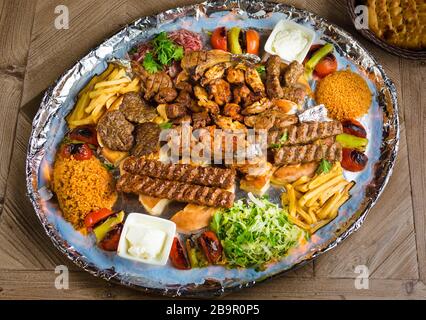 La vue du mélange Persique Kebab de viandes hachées et de poulet avec du riz et des frites et des légumes dans un grand bac en bois traditionnel sur table Banque D'Images