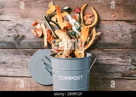 Légumes pelés sur la planche à découper, bac à compost blanc sur fond de bois. Vue de dessus des déchets alimentaires de cuisine collectés dans le recyclage du pot de compost Banque D'Images