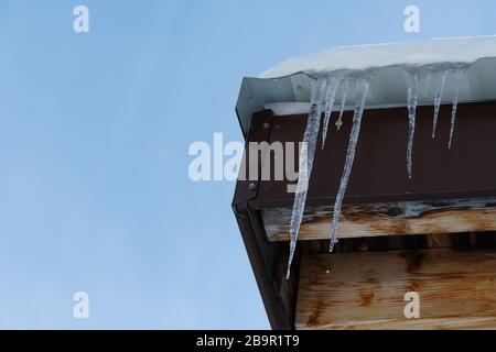 Glaces fondues suspendues à un coin du toit avec des gouttes d'eau tombant sur le fond du ciel bleu. Banque D'Images