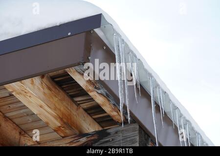 Des glaçons qui fondent sur un toit avec des gouttes d'eau tombant sur le fond du ciel bleu. Banque D'Images