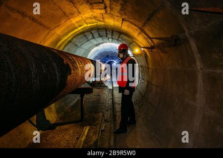 Le travailleur du tunnel examine le pipeline dans le tunnel souterrain. Banque D'Images