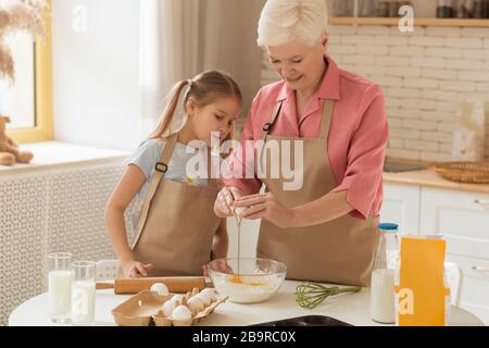 Cuisson ensemble. Une dame plus âgée et une jolie fille qui font de la pâte dans la cuisine Banque D'Images